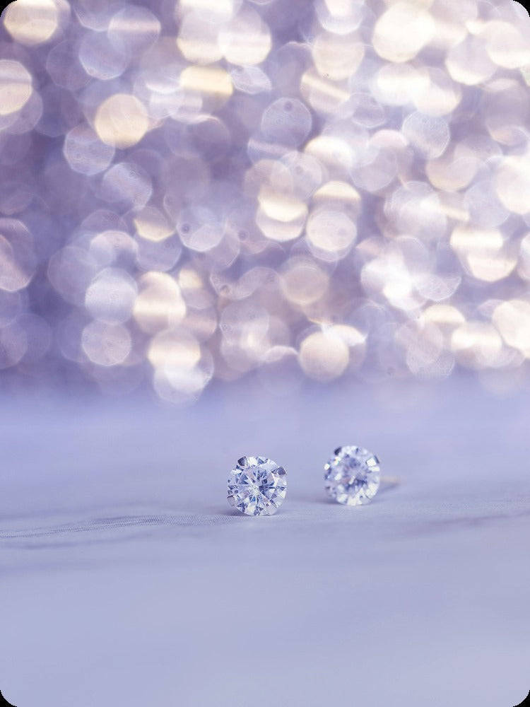 Diamond stud earrings on a light purple background with bokeh effect