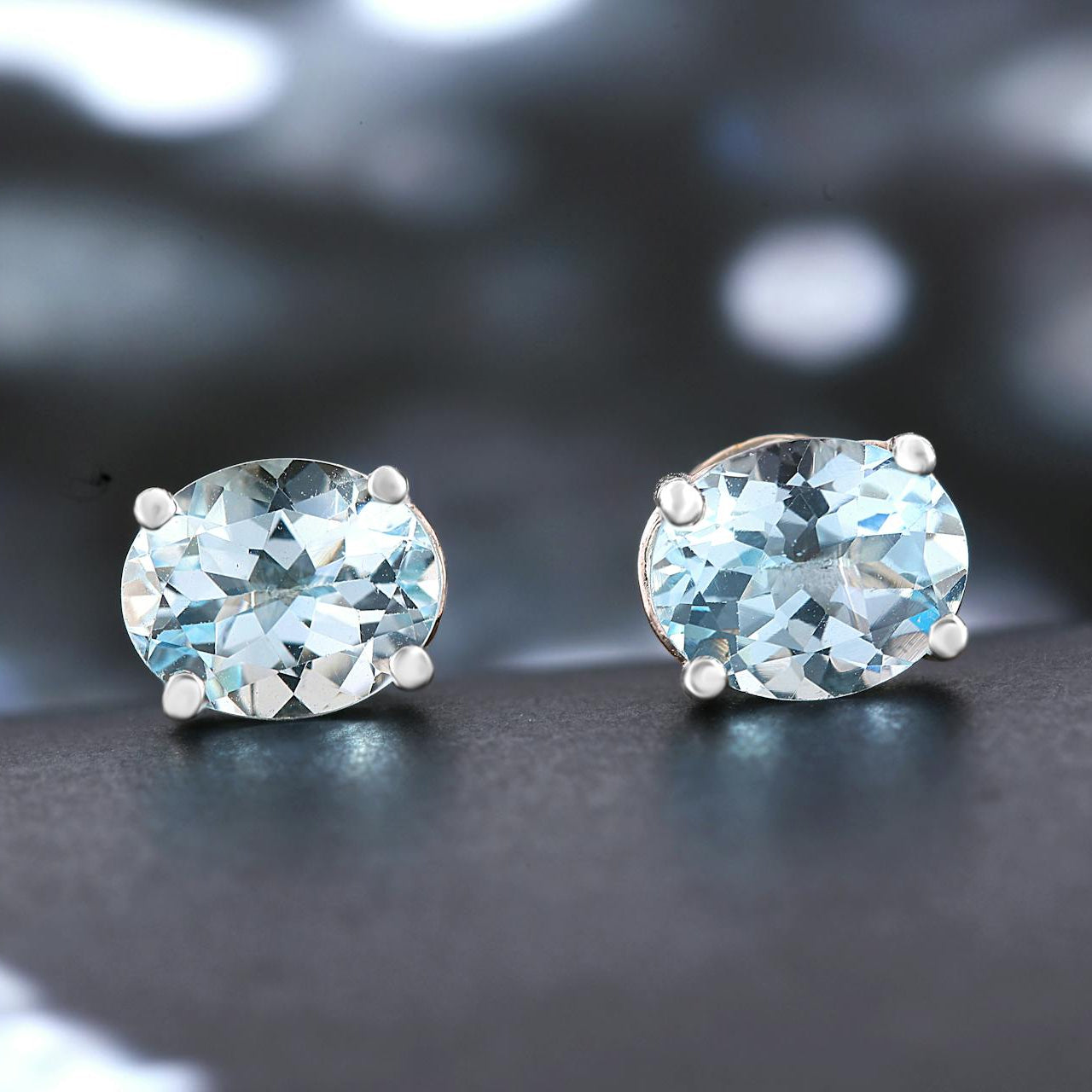 Pair of gemstone earrings on a reflective surface with a blurred background